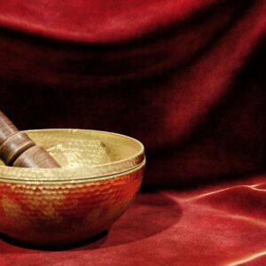 Brass bowl with a wooden mallet on a red velvet background.
